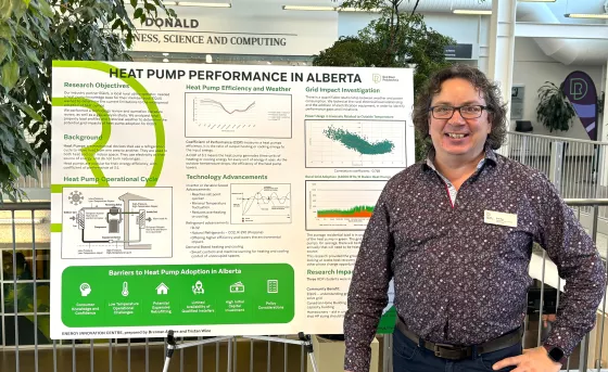 A researcher in a purple shirt stands with a hand on their hip, next to a presentation board that reads "heat pump performance in alberta"