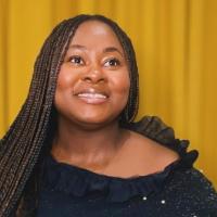 Oluwaseyifunmi smiles looking upwards. Her hair falls in long braids over her black dress.