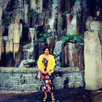 Zanaib stands in front of a large rock formation, wearing a flowered dress and yellow jacket.