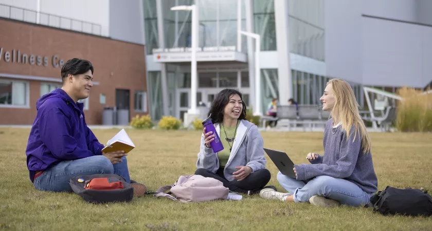 Three students sitting on grass outside Harris Centre
