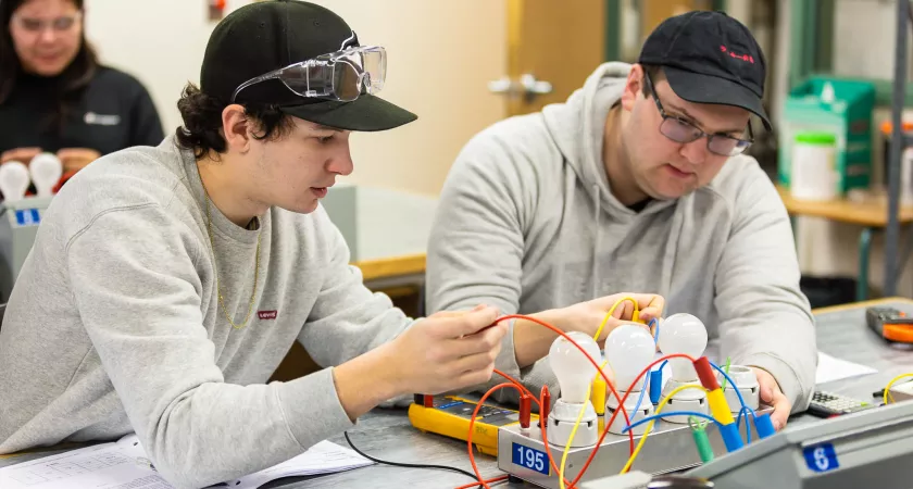 Two electrician students in a lab working with light bulb circuits.