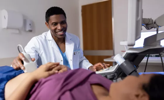 A sonographer smiles while using an ultrasound wand on a patient abdomen.