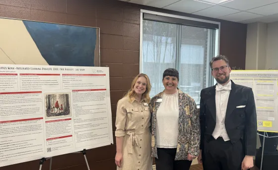 Three faculty members stand smiling besides posterboards that explain their research at the RoSA Awards