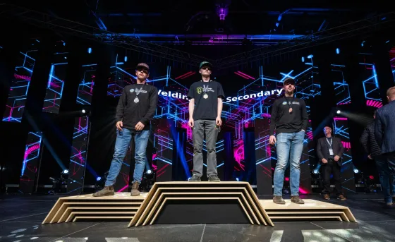 Lucas Stang (RDP Welding student) stands with his gold medal on a podium with two other welders at Skills Canada Alberta 2025