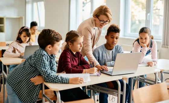 A group of youth learn with a teacher pointing to a laptop