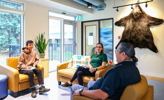 A group of three sit on comfortable looking couches at the Pónokaisissáhta Indigenous Student Centre