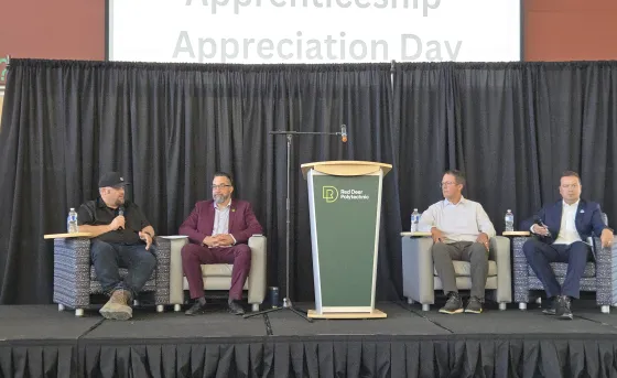 Members from the community and RDP sit on a stage with a sign that reads "Apprenticeship Appreciation Day"