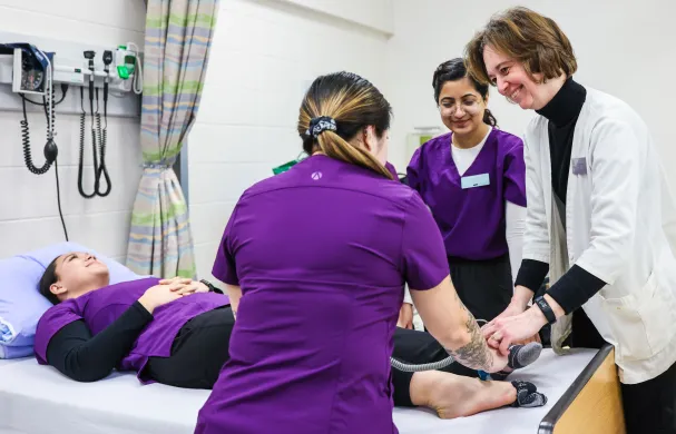 A group of student nurses and a faculty member practice their techniques on another student