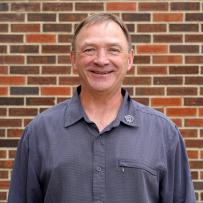 A smiling headshot of Bill Petrosenko in front of a brick wall