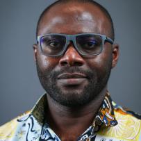 Isaac wears dark grey glasses and a vibrant shirt with various prints