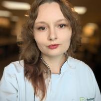 Miranda has long brown hair, wearing her chef's jacket and looks into the camera