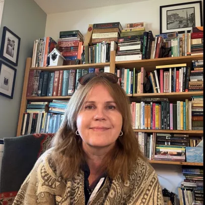 A smiling headshot of Tracy Kulba-Gibbons in front of a wall of books