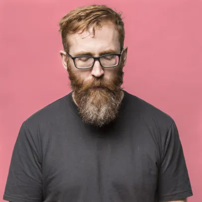 Robert Lambert against a pinkish backdrop, looks down at an artist's tool in his hands