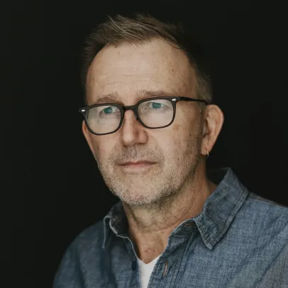 Carl looks pensively into the distance against a dark black background. 