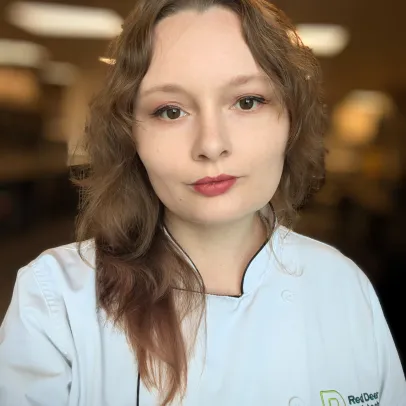 Miranda has long brown hair, wearing her chef's jacket and looks into the camera