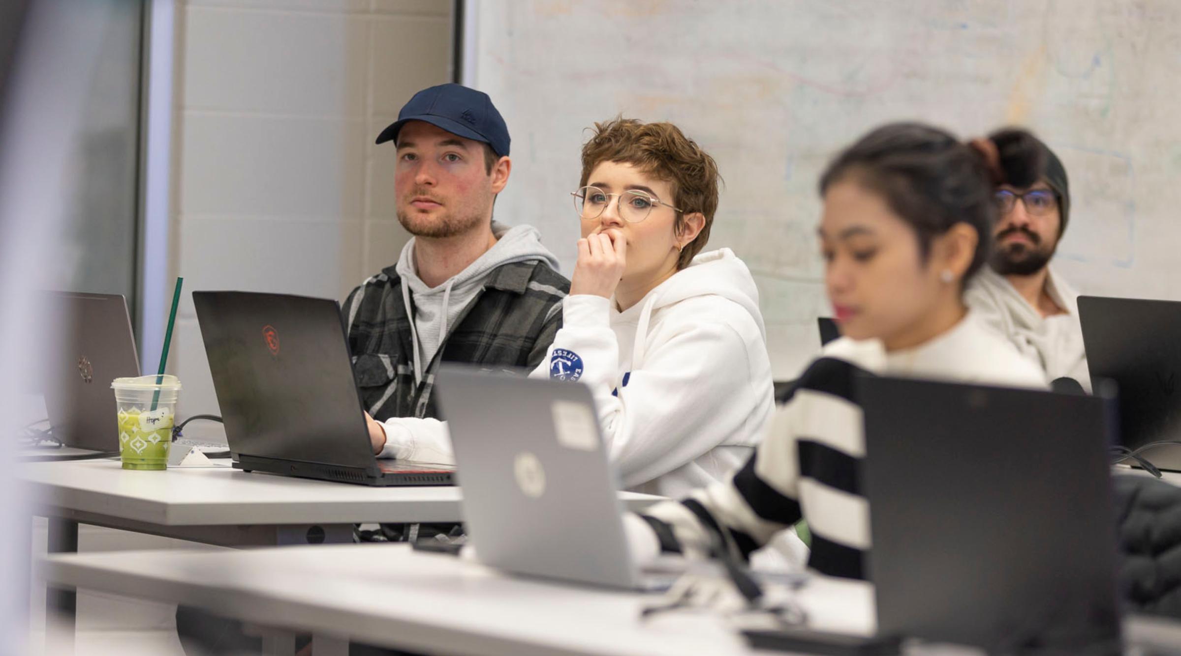 A group of three students on laptops look just off-camera looking very focused