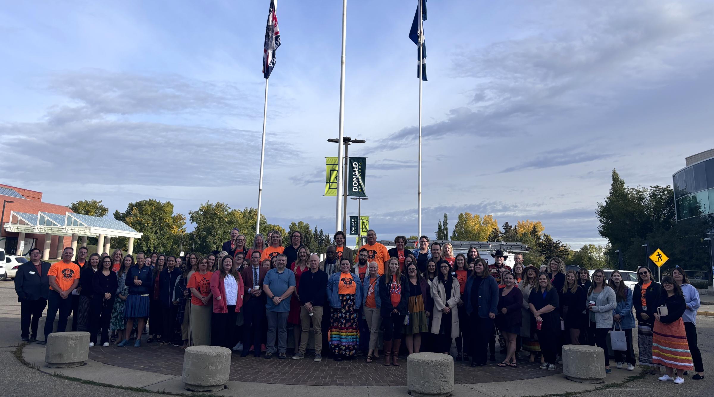 A group of RDP staff and students stand outside the front entrance as an Indigenous flag is raised