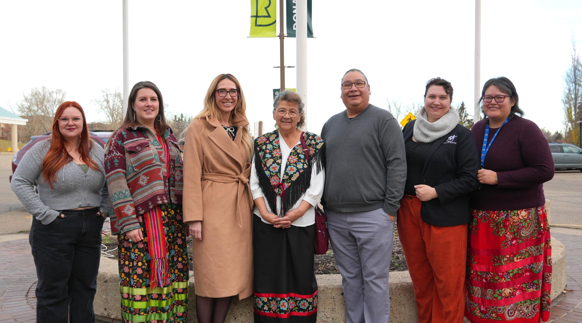 A group of RDP representatives and members of the Metis community stand in front of the raised Metis flag in front of RDP