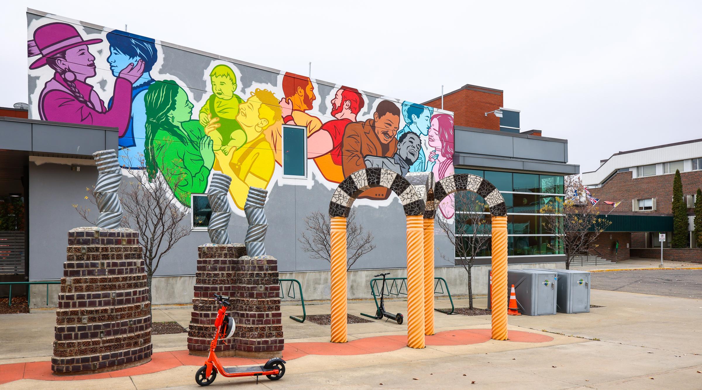 A mural celebrating Pride outside of the library. It features a diverse group of folks in the colours of the pride flag