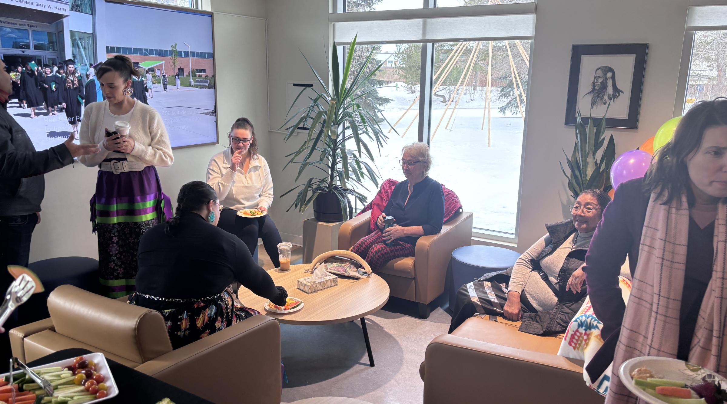 A group sits in front of a bright window inside the Pónokaisissáhta Indigenous Student Centre