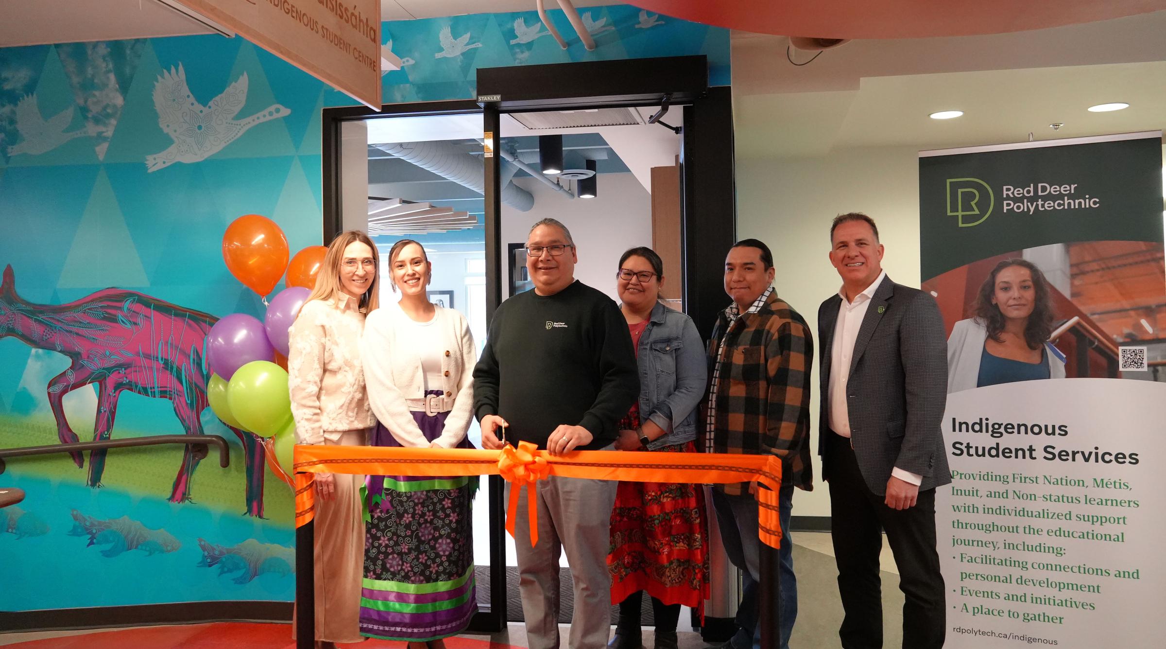 A group of RDP staff and students stand in front of an orange ribbon ready to cut it