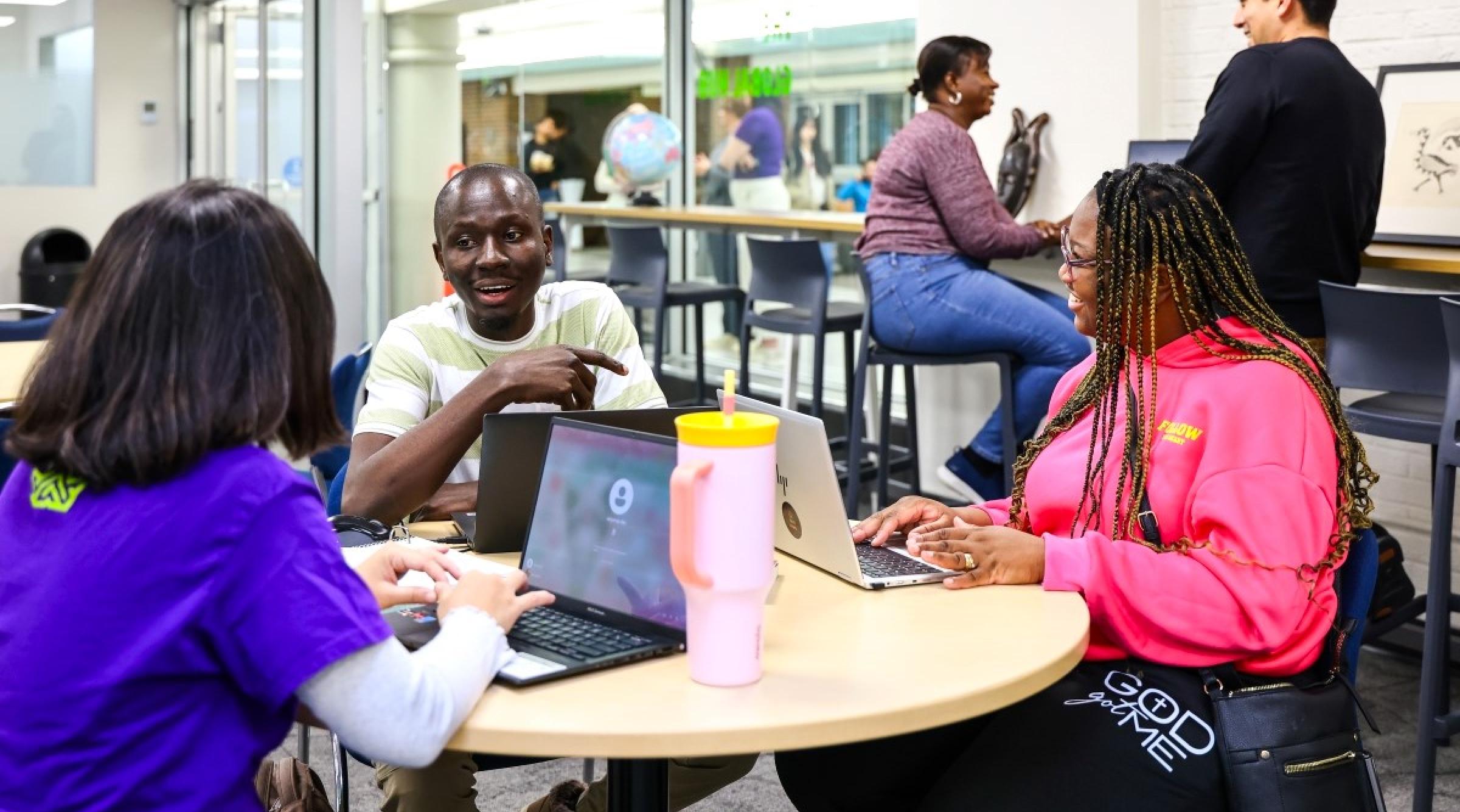 A group of diverse international students sit chatting and laughing at a table in RDP's Global Hub