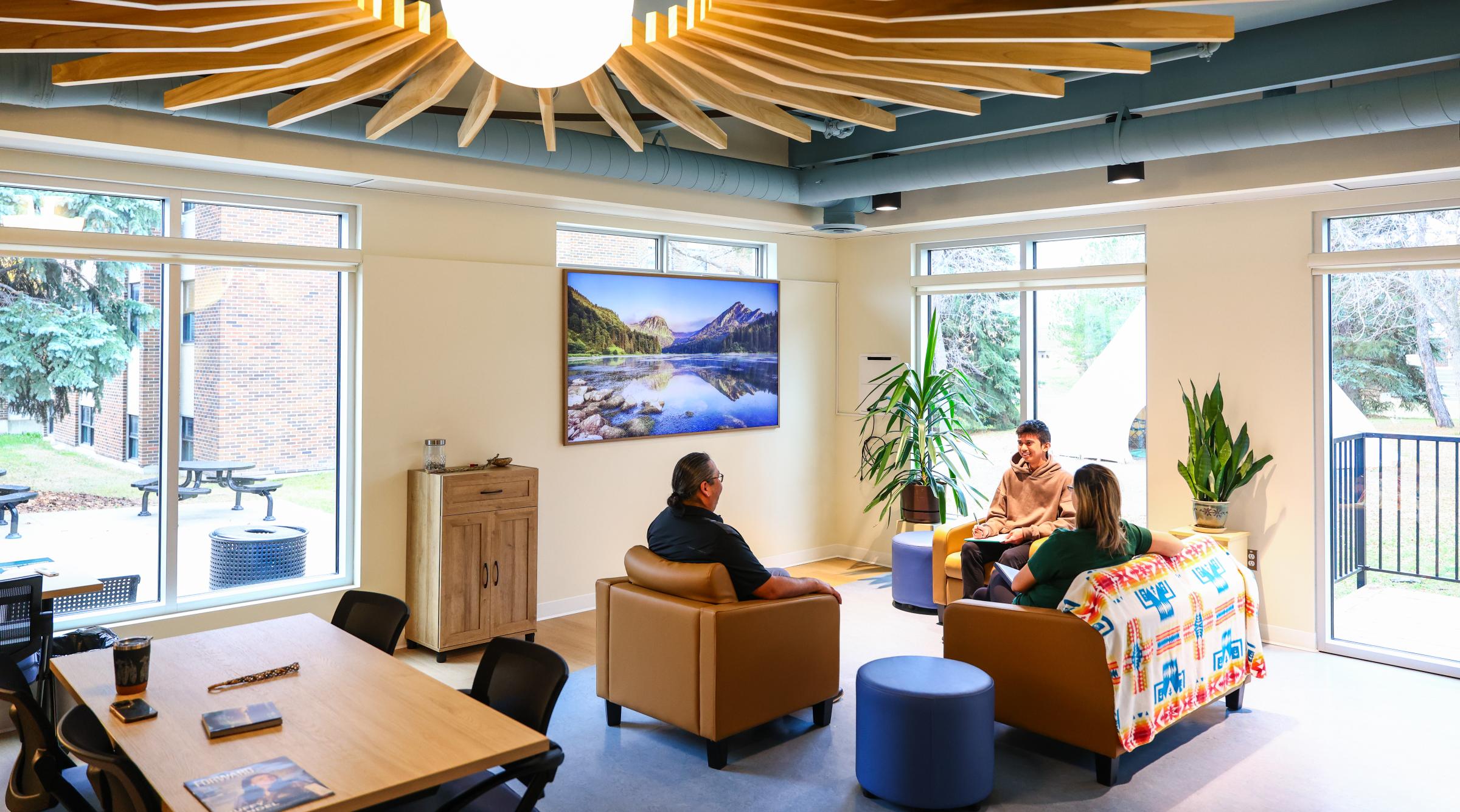 Three people sit inside the new Indigenous Student Centre. The space has dynamic architectural features on the roof and comfy seating