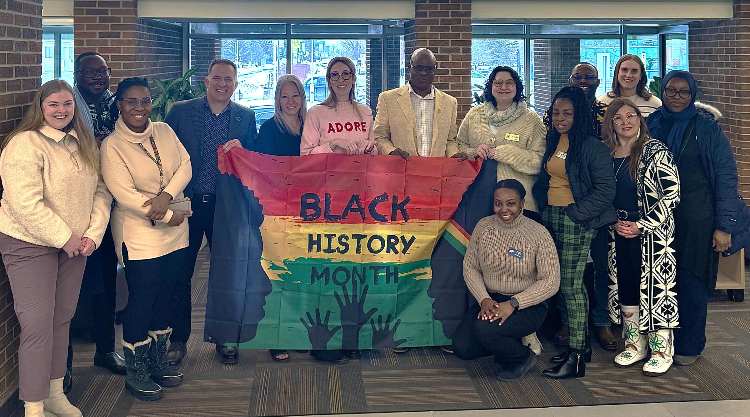 A diverse group of RDP's community holds up the Black History Month flag