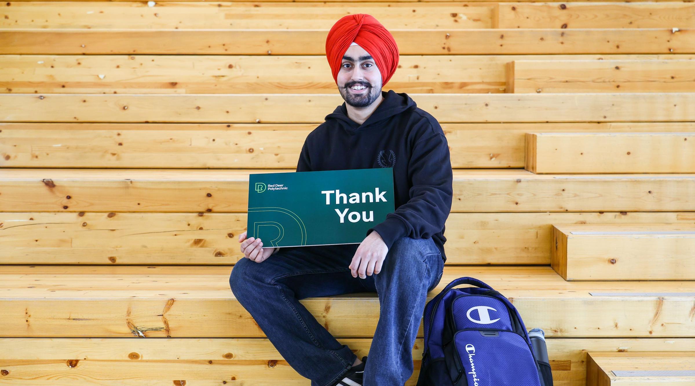 A smiling Sikh man holds a sign that reads "Thank You"