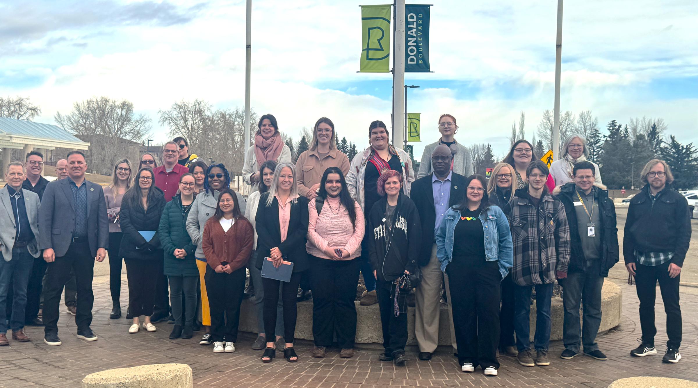 A group of RDP faculty, staff and students gather outside the flagpoles where the Pride flag has been raised