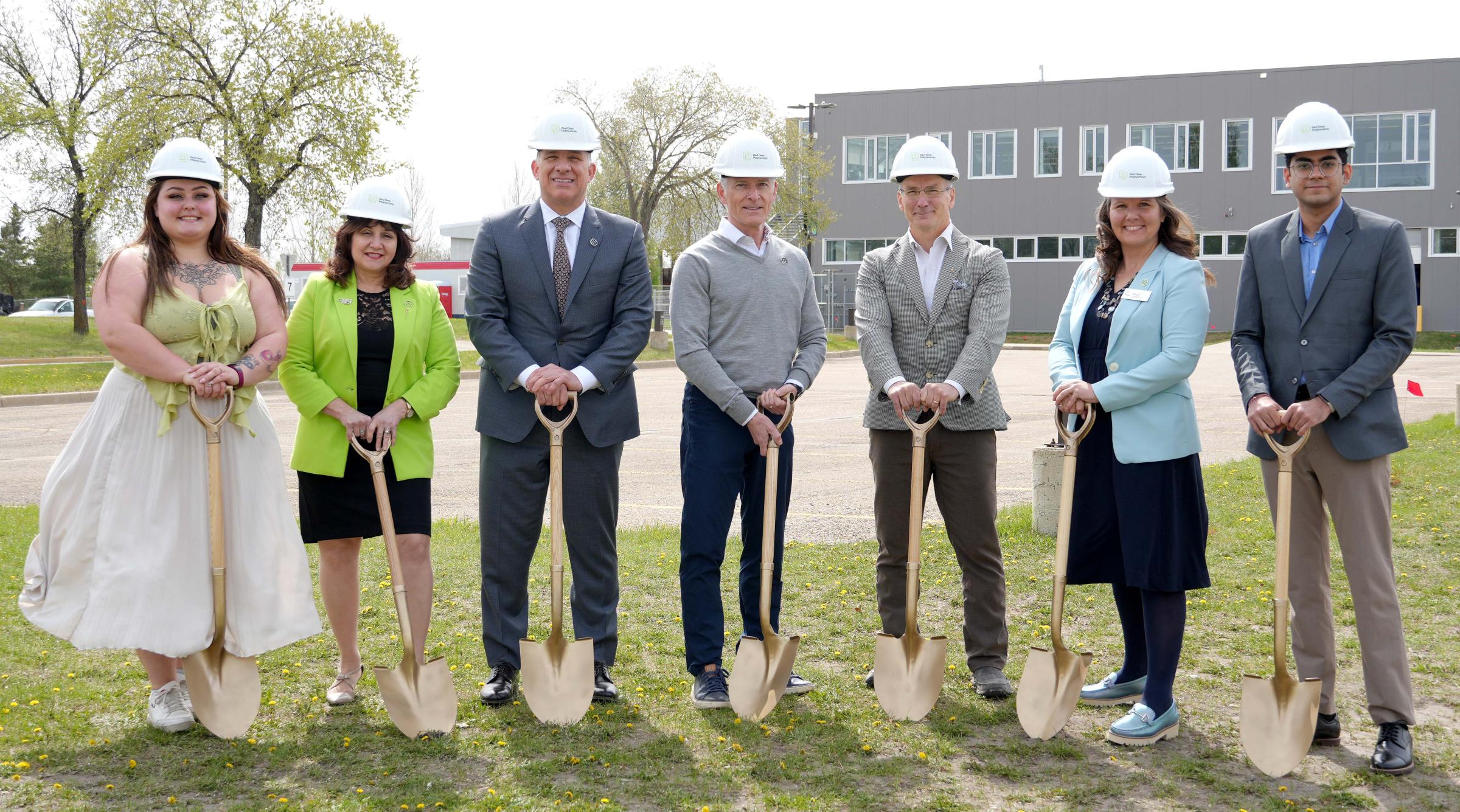 A group of RDP and Government of Alberta reps wear hardhats while holding shovels