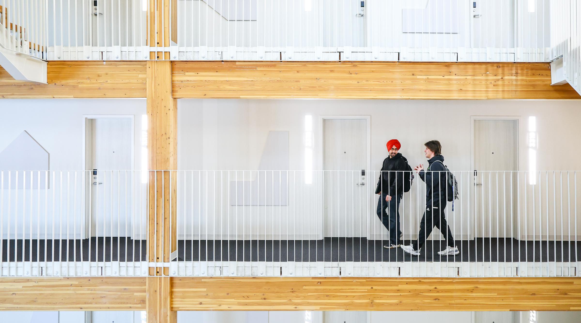 A wide shot of two male students walking in RDP's new residence. You can see multiple floors made of clean white walls and bright coloured wood.