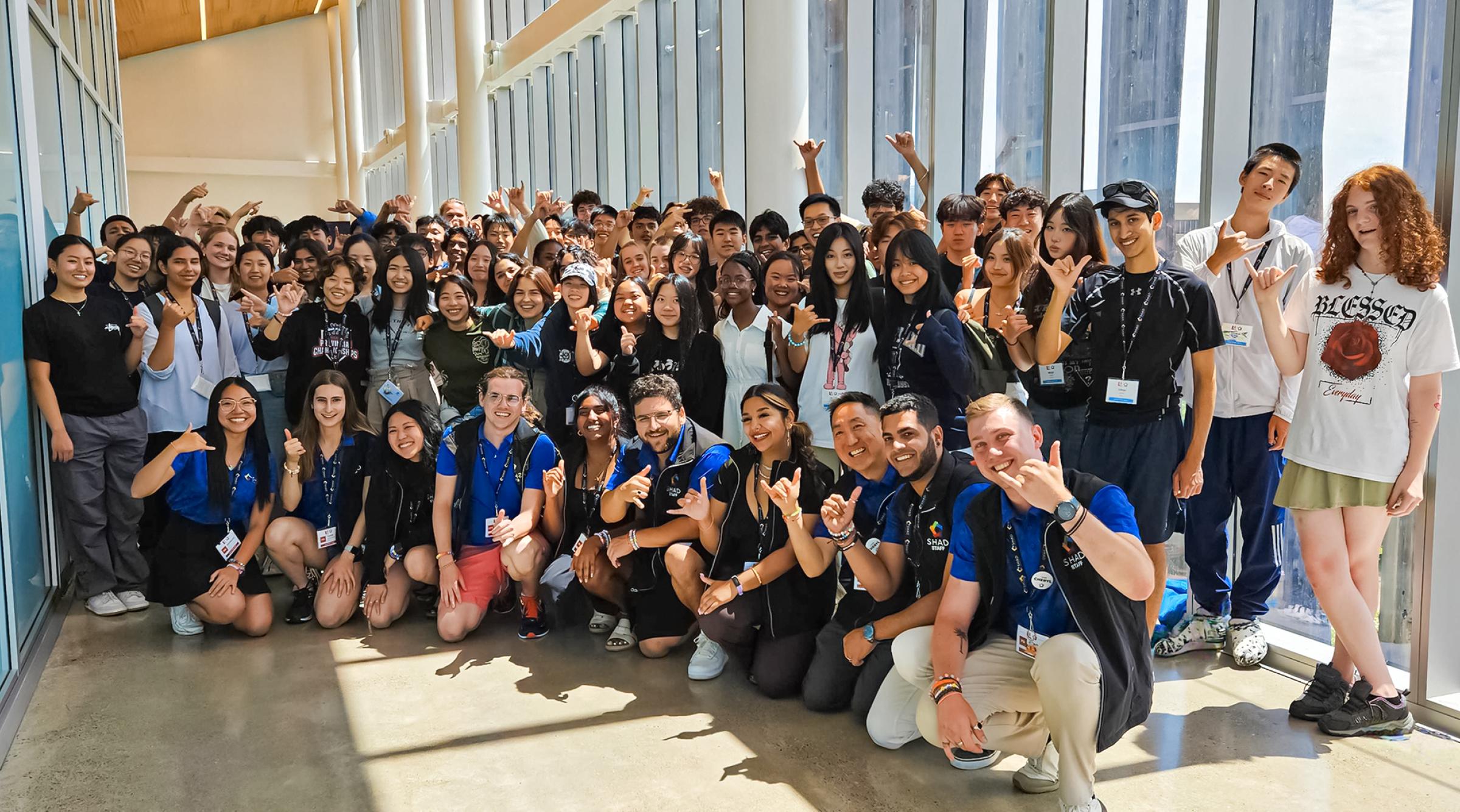 A large group of diverse high school students pose in a long corridor of windows