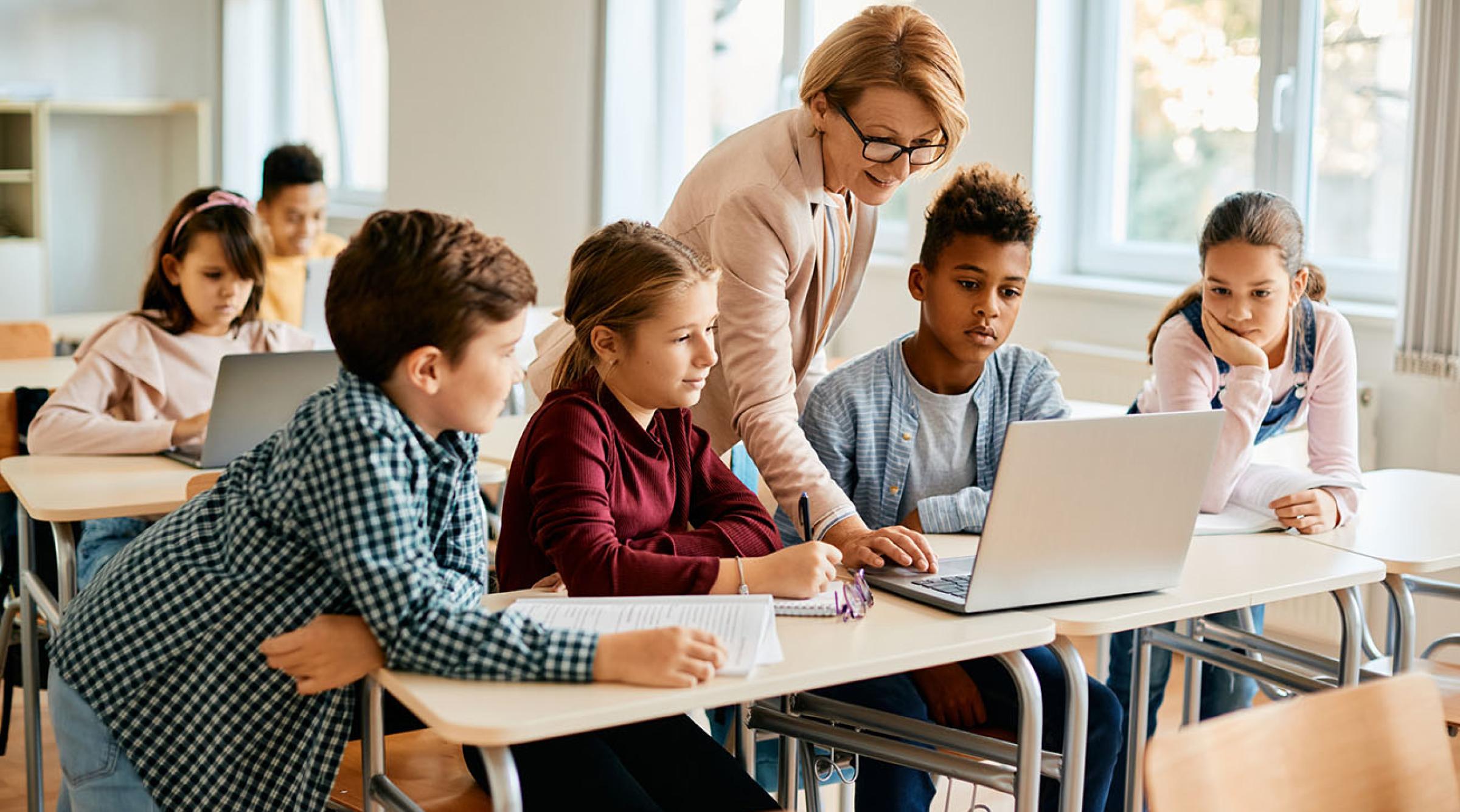 A group of youth learn with a teacher pointing to a laptop