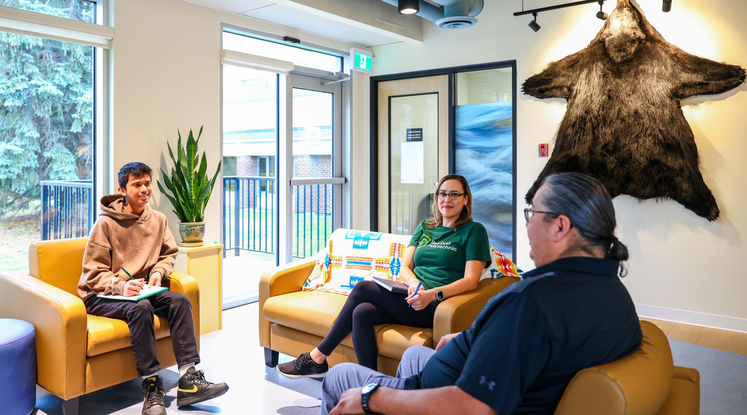 A group of three sit on comfortable looking couches at the Pónokaisissáhta Indigenous Student Centre