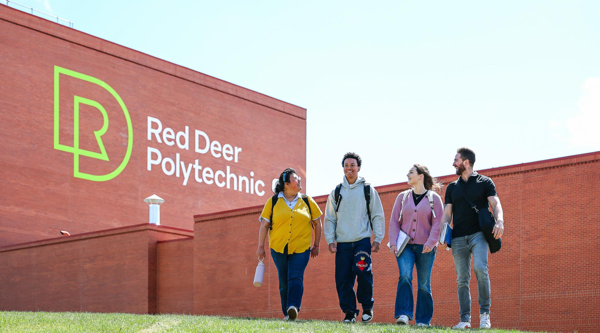 Four students walking together outside of campus on a green grass covered hill. The RDP logo is on the side of the brick building.