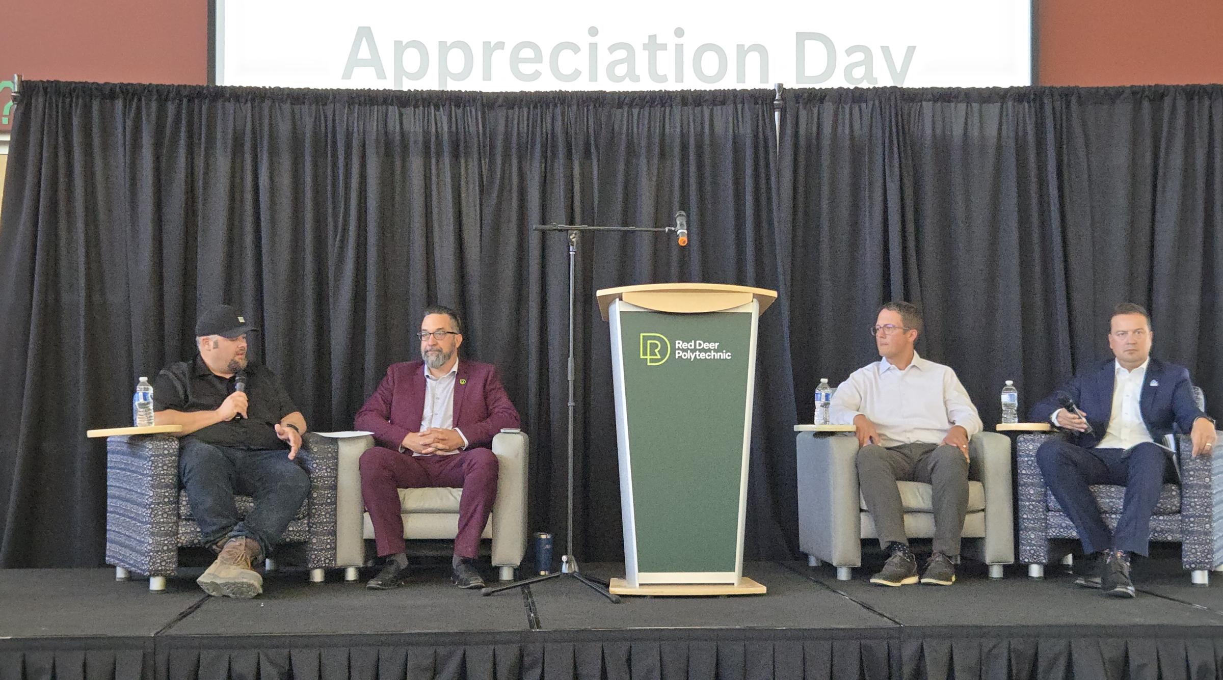 Members from the community and RDP sit on a stage with a sign that reads "Apprenticeship Appreciation Day"