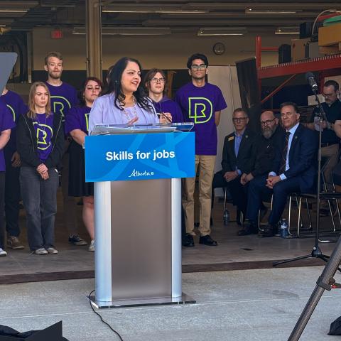 Rajan Sawhney addresses the crowd from a podium that reads "Skills for Jobs.". Behind her is a group of RDP students and staff.