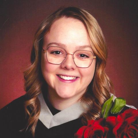 Graduation picture of a smiling Catrina Amendt in her grad gown holding a bunch of red roses