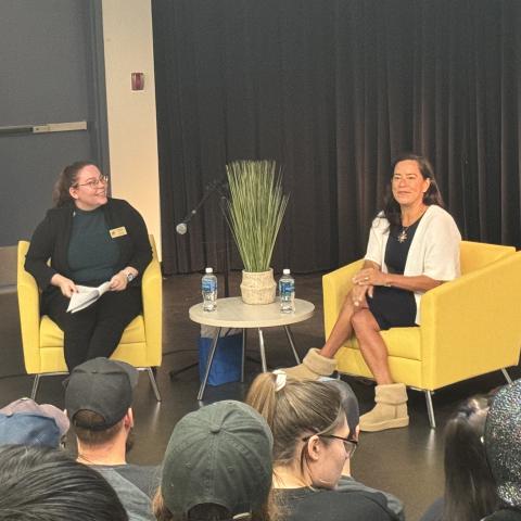 Jody Wilson-Raybould sits in a yellow armchair across from a host. She is looking happily out into a crowd full of students