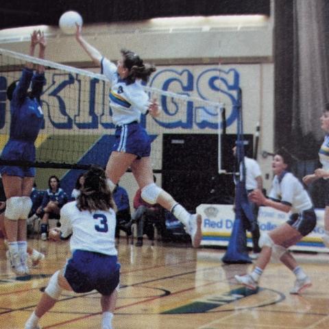 An archival photo of the Queens volleyball team. A player is in the middle of an impressive spike