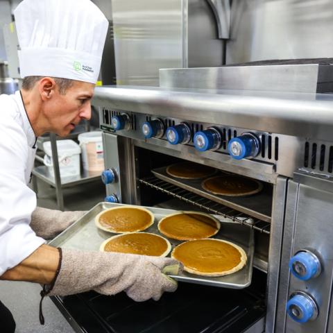 Garnett Shoettler, chair of the culinary programs at RPD, is taking pies out of a large oven while wearing chef attire