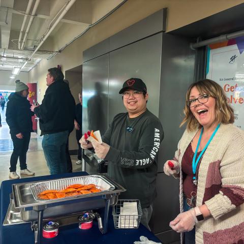 Two employees smile brightly as they serve up patties.