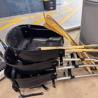 Three sledge hockey platforms in a pile with sledge hockey sticks ontop.