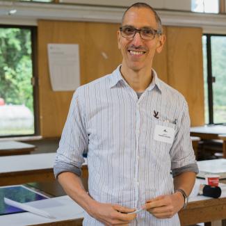 Joseph, wearing a striped white shirt and nametag, smiles in an art studio.