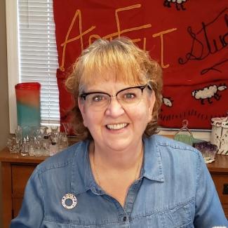 Leah wears a denim shirt and glasses in an art studio.