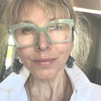 Jean wears a white button up top and green glasses.