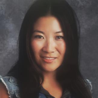 Monica in grey shirt with long black hair against a grey photo backdrop.