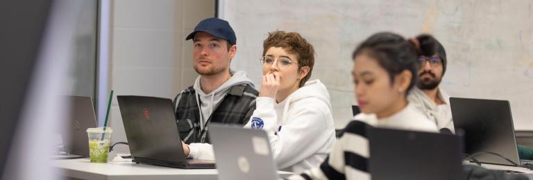 A group of three students on laptops look just off-camera looking very focused