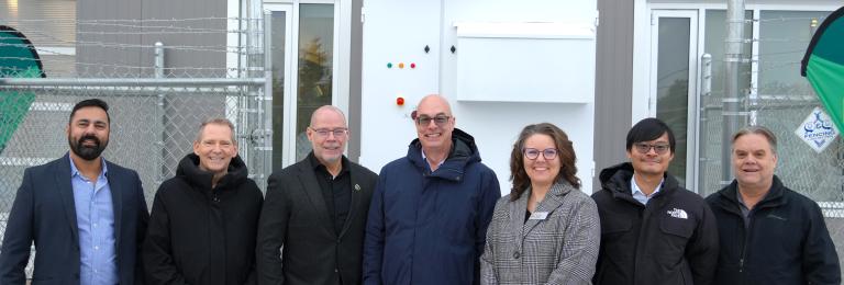 A group of representatives from RDP and Exro Technologies stands outside in front of the First Cell Driver Energy Storage System